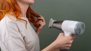 A woman with curly and colored hair blowing drying her hair.
