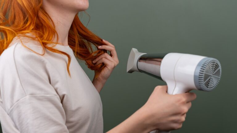 A woman with curly and colored hair blowing drying her hair.